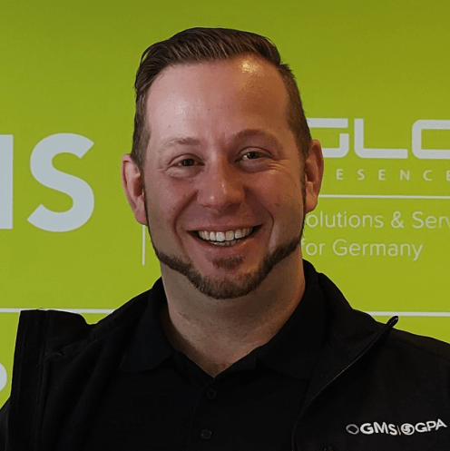 Ein Mann lächelt vor einer grünen Wand.